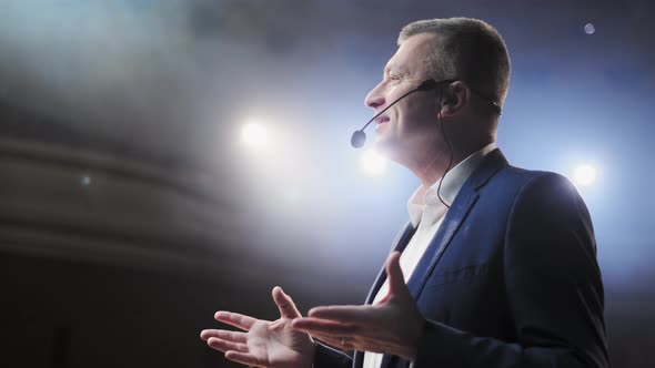 Portrait of Men Speaking Through a Microphone in Dark Conference Hall. Person Says About Marketing