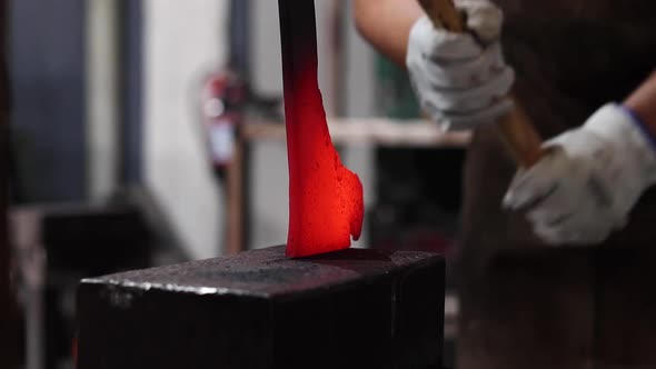 Blacksmiths forging hot metal with hammer in workshop