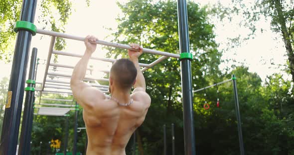 Back View of Male Athlete Doing Pullup on Horizontal Bar Outdoors While Using Street Gym Equipment alt