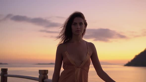 Portrait of Lovely Girl in Orange Sundress Posing with Pink Sunset Sky in the Background Looking