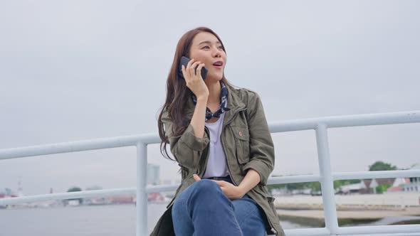 Asian attractive woman backpacker talking on mobile phone call while travel alone on ferry.