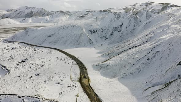 Aerial of Car Driving on Dirt Road Along the Snow Covered Mountains in Iceland