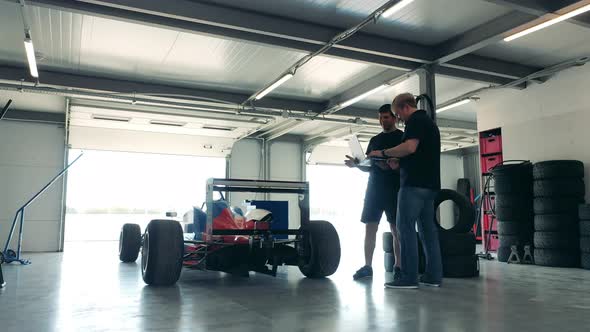 Two Specialists with a Laptop are Talking Next to the Racing Cart