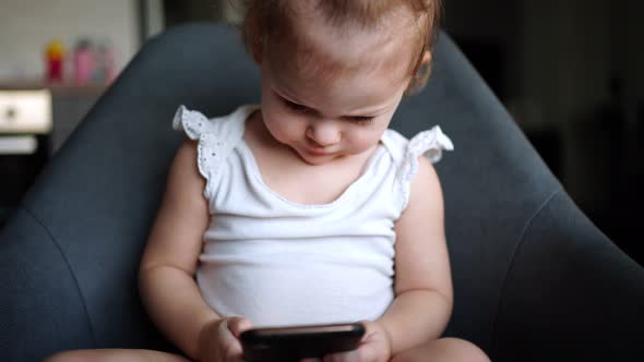 Smiling Little Girl is Sitting on Armchair and Using Smart Phone