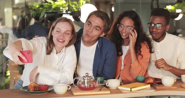 Young People Laughing and Waving While Having Video Call in Cosy Restaurant. Happy Girl Holding