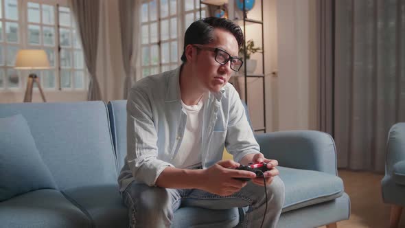 Bored Asian Man Using Joystick Playing A Game At Home