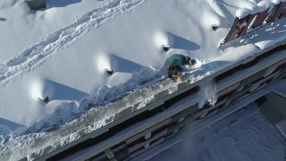 Man Ploughing The Snow At The Edge Of The Rooftop Of The Building In Zakopane, South Poland. aerial