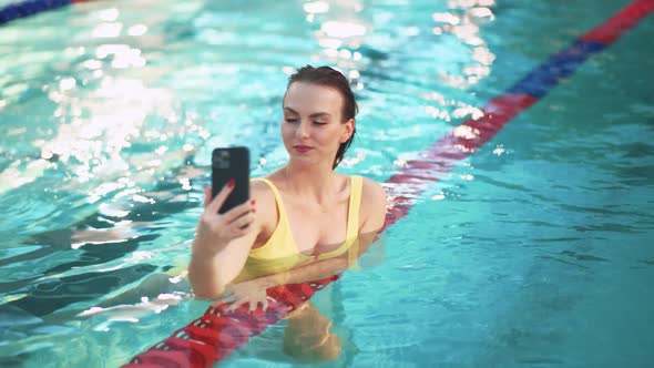 Females in the Pool Two Beautiful Girls in Yellow Swimsuits Take a Selfie on a Smartphone While in