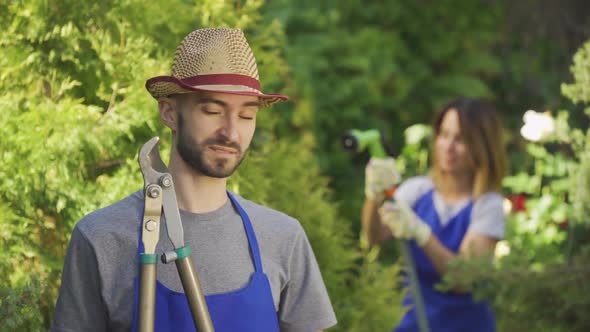 Handsome Young Farmer in Blue Robe Standing in the Foreground While His Wife Watering Trees