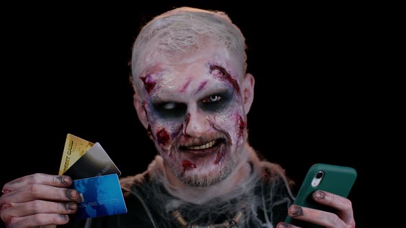 Sinister Man Halloween Zombie Using Credit Bank Cards and Smartphone While Purchases Online Shopping