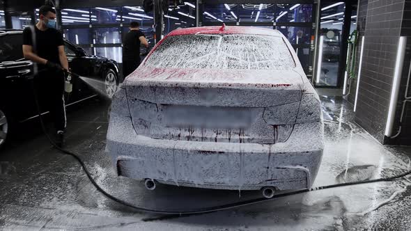 A Man Covers the Car with a Layer of Foam Using a Sprayer