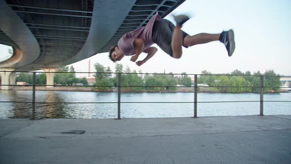 Training of a Parkourist or Freerunner Under a Bridge on the Background of a Pond and Linear