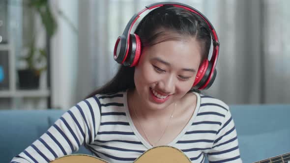 Close Up Of Asian Woman Composer Wearing Headphones And Playing Guitar At Home