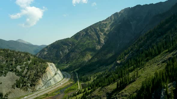 Flying above a highway far down in the canyon below the forested mountain peaks