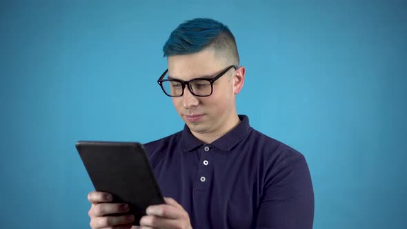 Young Man in Glasses with Blue Hair with a Tablet in His Hands. Alternative Man Is Writing in a