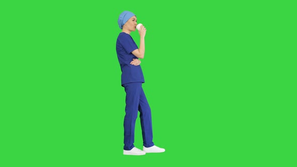 Smiling Female Doctor or Nurse in Blue Uniform Having a Coffee Break on a Green Screen, Chroma Key.