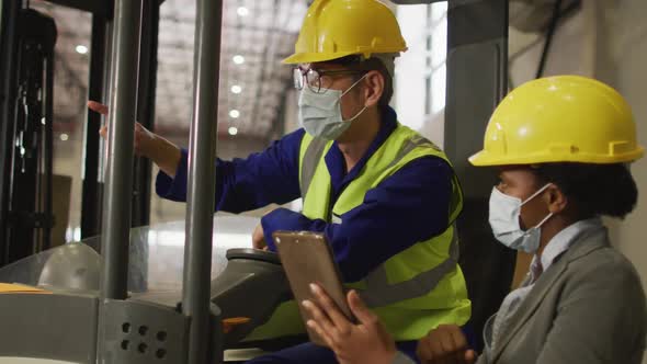 Diverse male and female workers wearing face masks and using tablet in warehouse