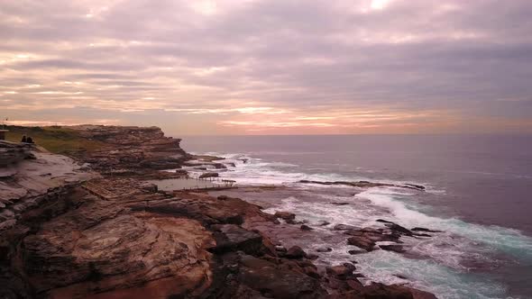 Aerial shot of velvet sunrise at the beach in a cloudy windy morning. Waves crashing on rocks. Sydne