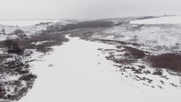 Drone flying over frozen ice lake with men fishing in ice hole