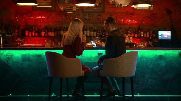 A Bewitching Couple Having a Date in the Bar - Sitting By the Stand and Looking at the Pictures in