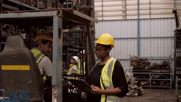 Black female engineer in safety uniform and Caucasian male forklift driver in warehouse factory.