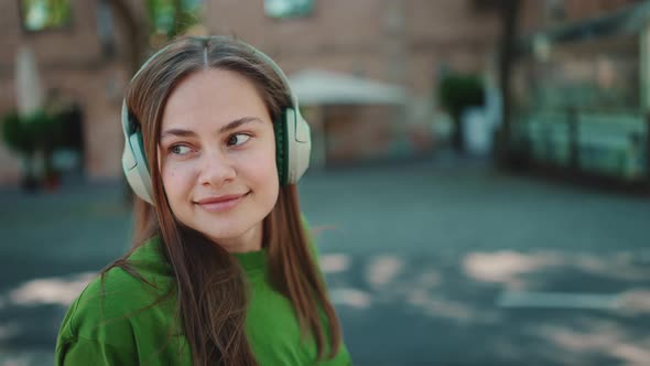 Pretty blonde woman wearing green t-shirt listening music in headphones and looking around