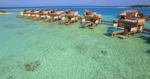 Aerial drone view of a man and woman couple with seascooters snorkeling near overwater bungalows.