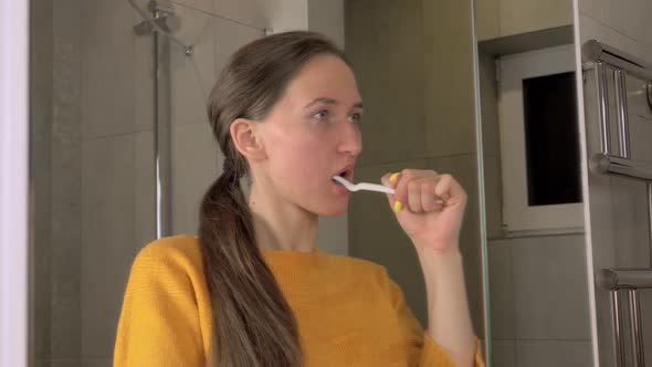 woman is reflected in mirror brushes her teeth with toothbrush and toothpaste
