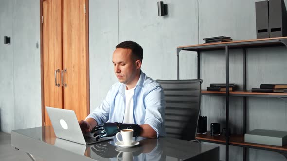 Concentrated man hacker with black bio hand prothesis types on grey laptop