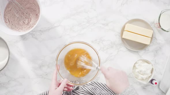 Flat lay. Step by step. Mixing wet ingredients in a glass mixing bowl to bake red velvet cupcakes.