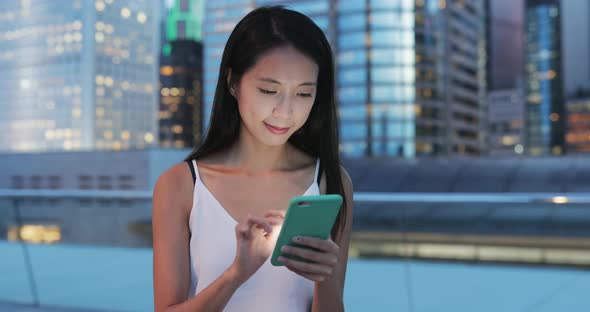 Woman typing on smart phone in city at night 