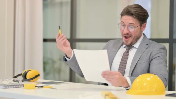 Middle Aged Engineer Celebrating Success while Reading Documents in Office