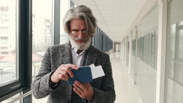 Elegant Senior Man Checking Passport and Bording Pass at Corridor in the Airport