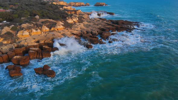 Aerial push out view of waves washing over cliffs at Algarve coast at golden hour