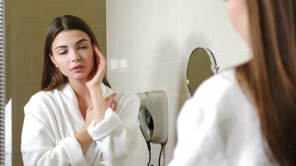 Portrait of Young Female Hotel Guest in White Bathrobe Looking at Herself in Mirror