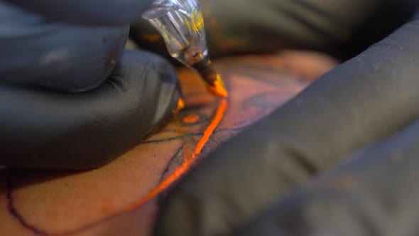 A Tattoo Artist Carefully Putting The Orange Color On His Tattoo Art Design While Wearing His Black