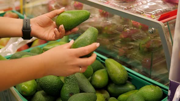 Closeup of a Young Woman Choosing a Fresh Avocado in a Grocery Store