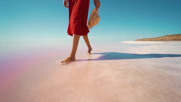 Woman Legs in Red Skirt Walking on Salt White Beach Holding Straw Hat