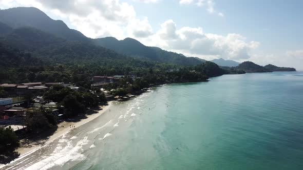 The green hills of the island are covered with palm trees, the sky is cloudy