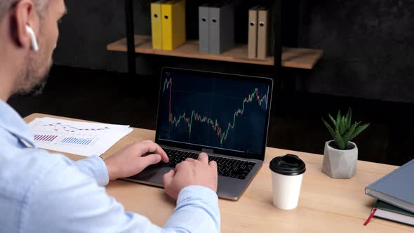 Adult Man Stock Trader Broker Uses Laptop with Stock Exchange Chart in Office