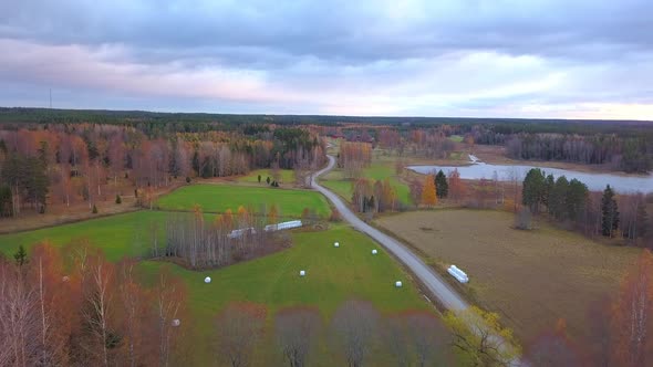 Aerial drone shot, over the countryside, towards colorful autumn trees and a lake, on a cloudy fall