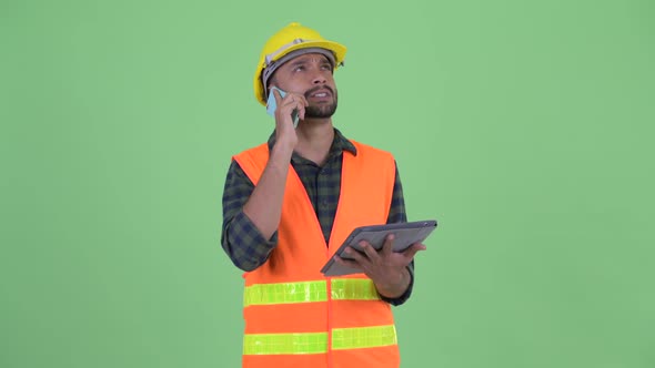 Happy Young Bearded Persian Man Construction Worker Using Phone and Digital Tablet
