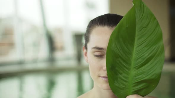 Young woman holding large leaf in front of her face, portrait