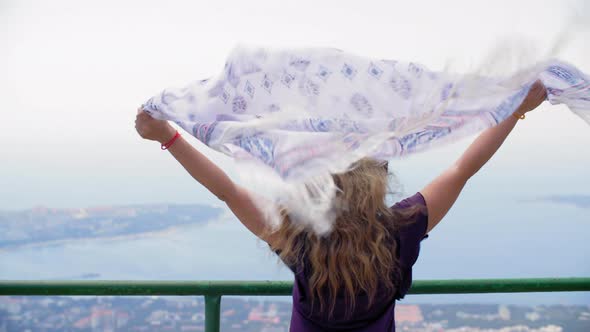 Happy Woman with Waving Shawl on Wind Standing Mountain Viewpoint with Seascape. Traveling Woman on