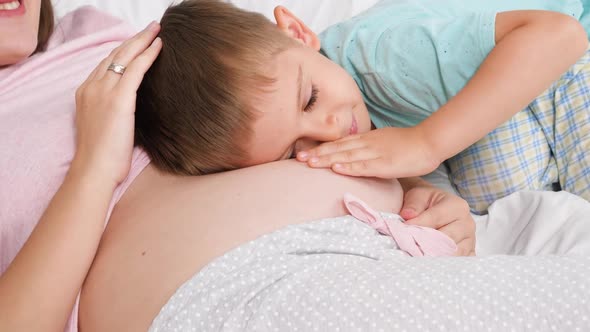 Portrait of Cute Smiling Toddler Boy Hugging and Stroking His Pregnant Mother with Big Belly