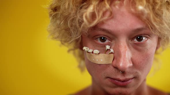 Headshot of Redhead Queer Man with Brown Eyes and Medical Patch Holding White Flowers Posing at