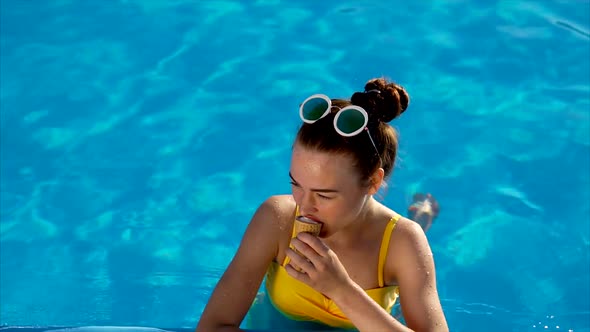 Young Woman Eats Appetizing Creamy Ice Cream in a Horn She is in a Swimming Pool