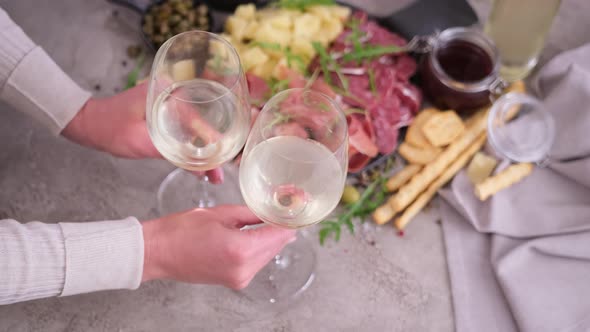 Woman Putting Two Glasses of Wine to Table with Meat and Cheese Plater at Domestic Kitchen