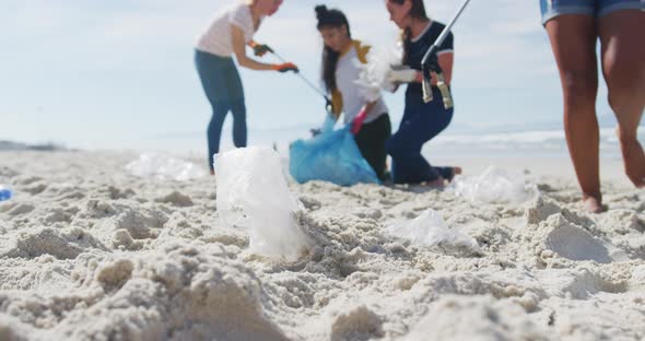 Diverse group of female friends putting rubbish in refuse sacks at the beach