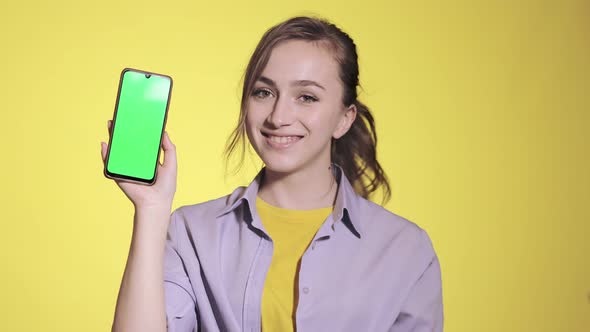 Charming young woman pointing at green screen on smartphone
